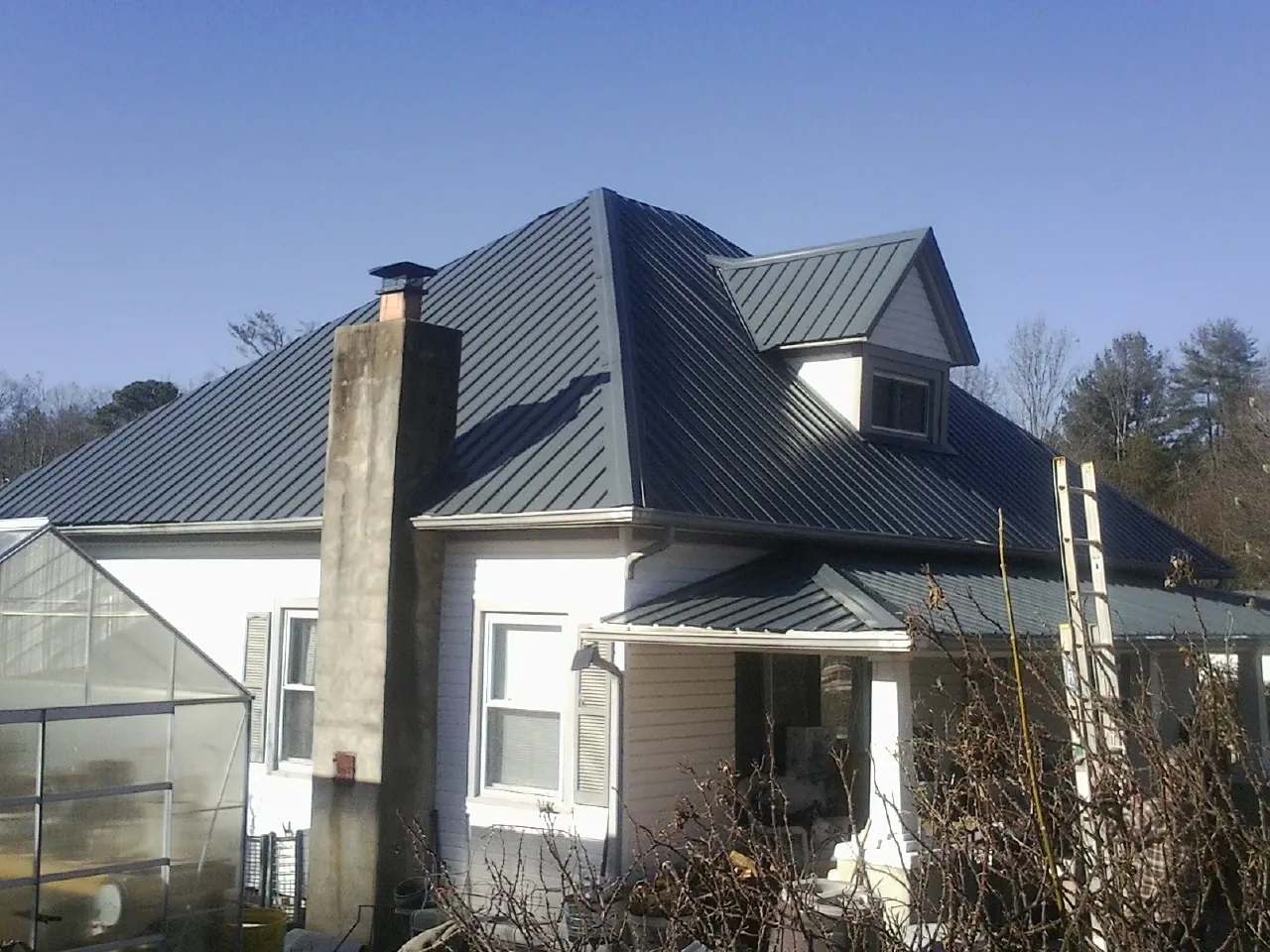 Dark blue standing seam metal roof on a white farmhouse with dormer — Slate & Tile Roof Repair by Roofing Brothers in Parmele