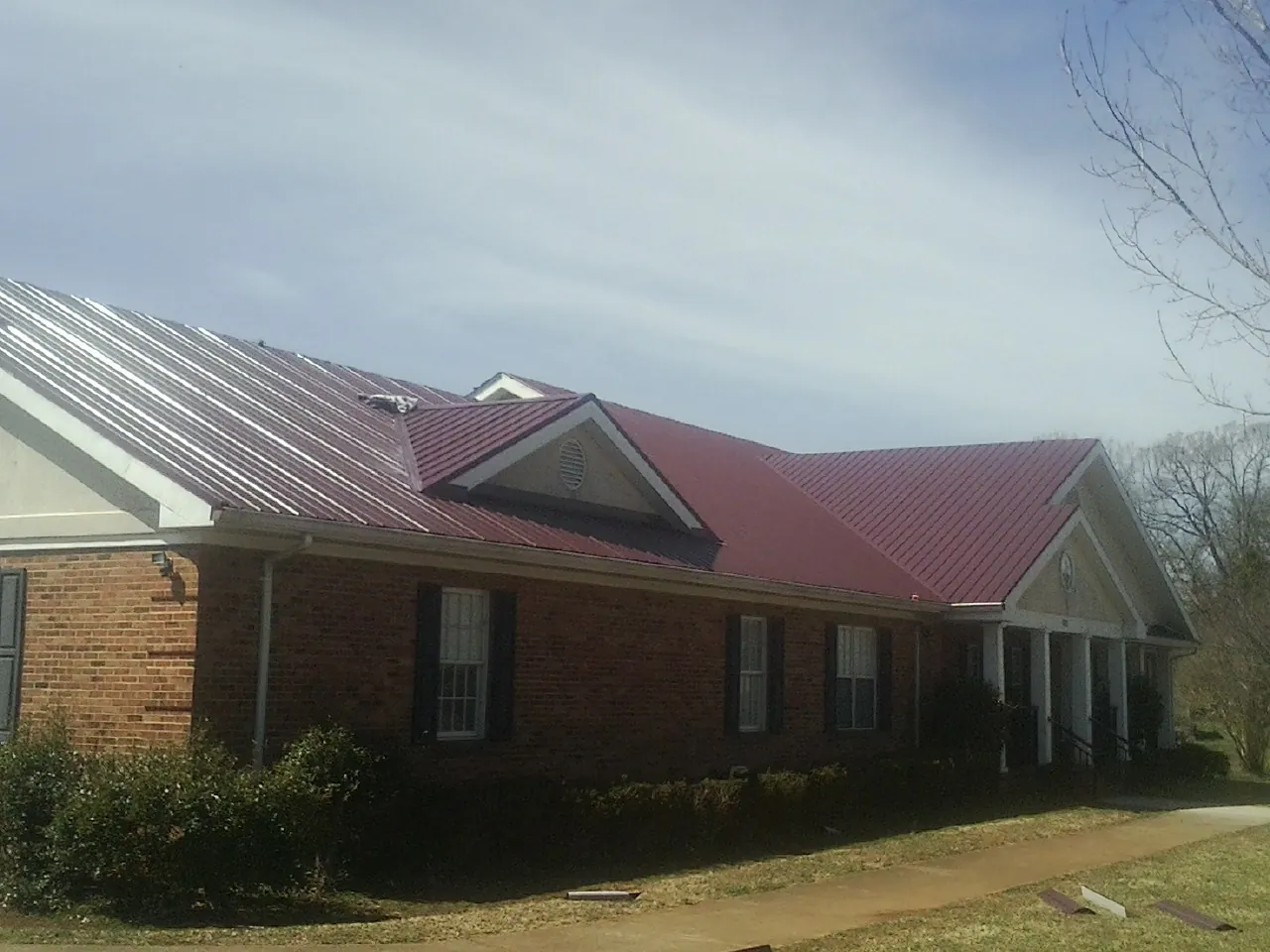 Red metal roof with gabled entries on a long brick building, from a Hail Damage Roof Repair job in Parmele