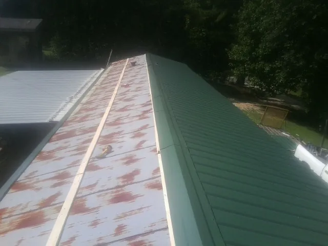 Old rusted panels beside newly installed green metal roofing — Wind Damage Roof Repair by Roofing Brothers in Parmele