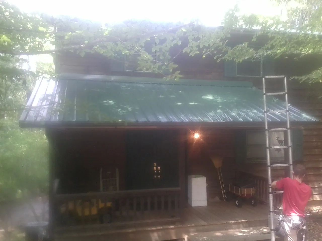 Worker on a ladder at the green porch roof of a wooded cabin in Parmele