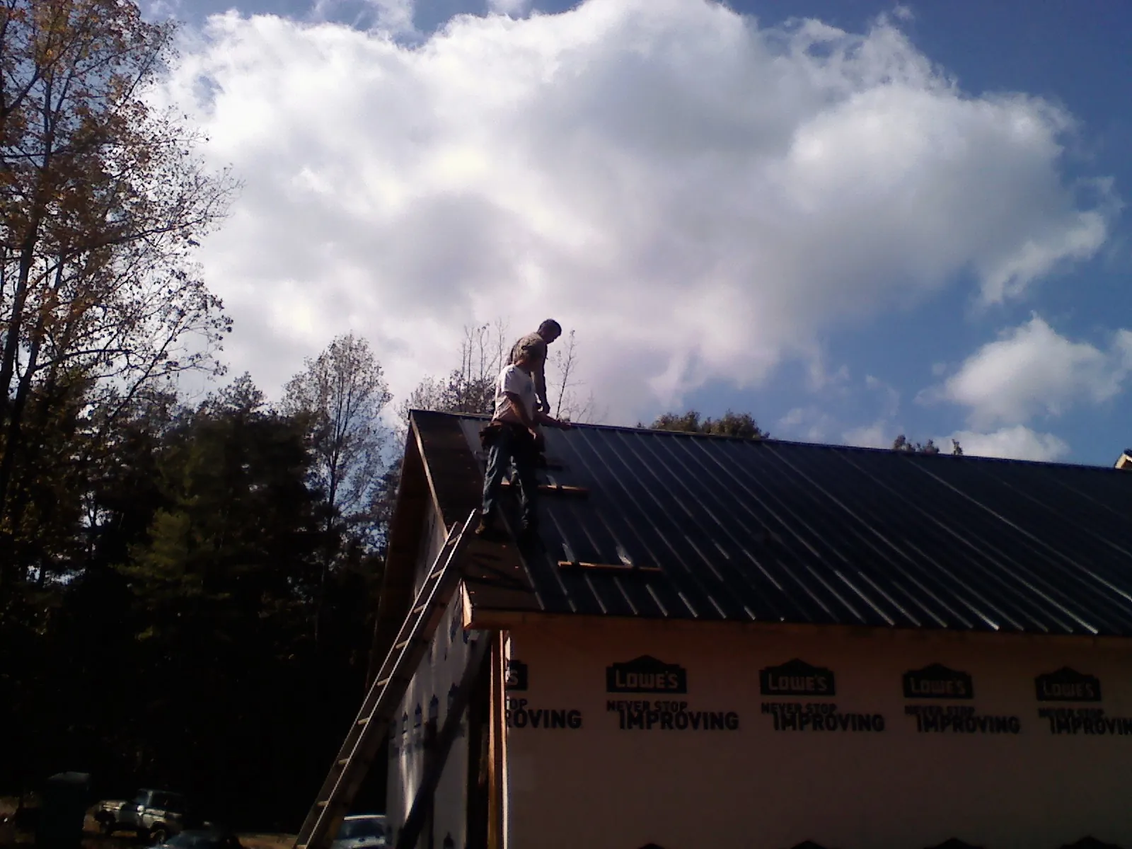 Roofer fastening dark metal panels high against a cloudy sky, from a Roof Inspection job in Parmele