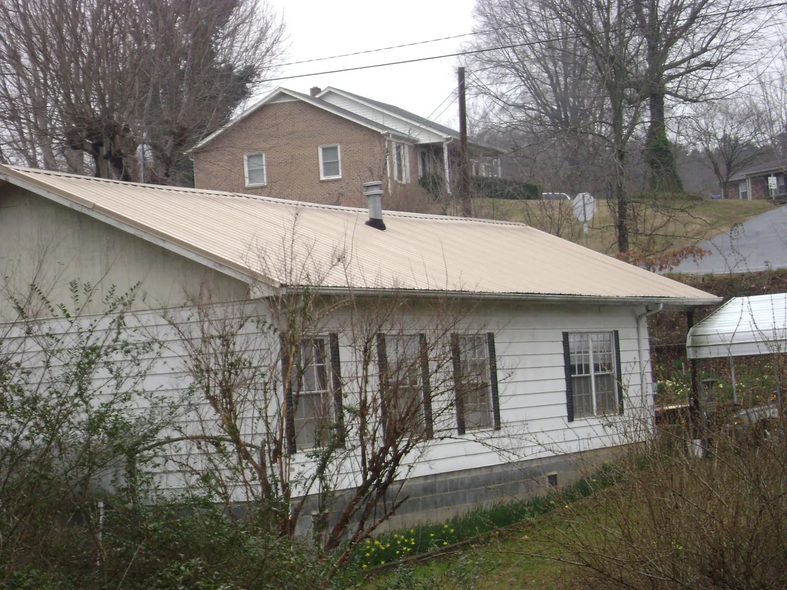 Tan metal roof on a white sided house set into a hillside — Commercial Roofing by Roofing Brothers in Parmele