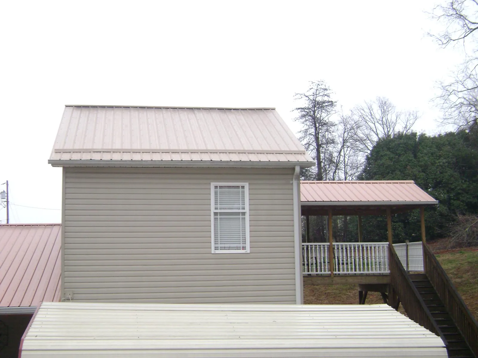 Tan metal roofs on a two story addition and attached porch, from a Roof Replacement job in Parmele